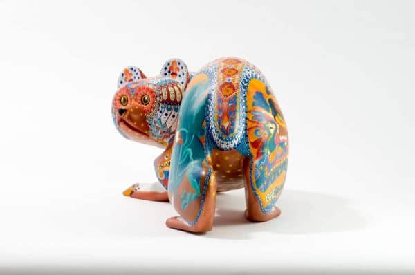 bear mexican wood carving alebrije This incredible bear carving by Ray Medez has intricate painting featuring pre-hispanic iconography and symbolism. Each of the four legs has an illustration. The front left leg shows the Aztec God Quetzalcoatl (represented by the feathered snake). The back right leg shows Kukulcn, the Mayan wisdom deity related to Quetzalcoatl.The front right leg depicts the Water-Lily Jaguar, an anthropomorphic form of an important Maya god. His special attribute is a water-lily atop his head, which may reflect the jaguarÕs love of water. This jaguar god moves and acts like a human. His necklace is called a death-eye collar and is part of his attire for the sacrificial death dance. The Water-Lily Jaguar is a significant character in Maya narrative artwork.The scene on the back left leg represents the extraction of the spirit beverage pulque from the maguey plant. The seashells on the body represent fertility and birth. It is also a symbol related to Quetzalcoatl.Extraordinary Mexican art from MexArt, London UK.