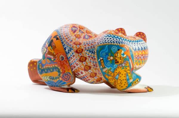 bear mexican wood carving alebrije This incredible bear carving by Ray Medez has intricate painting featuring pre-hispanic iconography and symbolism. Each of the four legs has an illustration. 
The front left leg shows the Aztec God Quetzalcoatl (represented by the feathered snake). 
The back right leg shows Kukulcán, the Mayan wisdom deity related to Quetzalcoatl.
The front right leg depicts the Water-Lily Jaguar, an anthropomorphic form of an important Maya god.  His special attribute is a water-lily atop his head, which may reflect the jaguar’s love of water.  This jaguar god moves and acts like a human.  His necklace is called a death-eye collar and is part of his attire for the sacrificial death dance.  The Water-Lily Jaguar is a significant character in Maya narrative artwork.
The scene on the back left leg represents the extraction of the spirit beverage pulque from the maguey plant. 
The seashells on the body represent fertility and birth. It is also a symbol related to Quetzalcoatl.
Extraordinary Mexican art from MexArt, London UK.