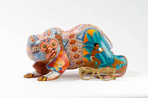 bear mexican wood carving alebrije This incredible bear carving by Ray Medez has intricate painting featuring pre-hispanic iconography and symbolism. Each of the four legs has an illustration. 
The front left leg shows the Aztec God Quetzalcoatl (represented by the feathered snake). 
The back right leg shows Kukulcán, the Mayan wisdom deity related to Quetzalcoatl.
The front right leg depicts the Water-Lily Jaguar, an anthropomorphic form of an important Maya god.  His special attribute is a water-lily atop his head, which may reflect the jaguar’s love of water.  This jaguar god moves and acts like a human.  His necklace is called a death-eye collar and is part of his attire for the sacrificial death dance.  The Water-Lily Jaguar is a significant character in Maya narrative artwork.
The scene on the back left leg represents the extraction of the spirit beverage pulque from the maguey plant. 
The seashells on the body represent fertility and birth. It is also a symbol related to Quetzalcoatl.
Extraordinary Mexican art from MexArt, London UK.